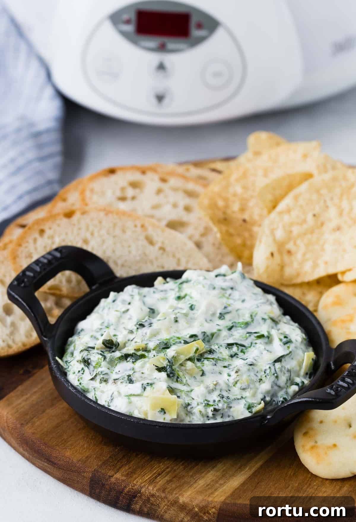 Small black bowl of dip on a wooden board with chips and bread.