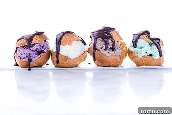 Row of four Gluten-Free Profiteroles stuffed with different colors of ice cream and drizzled with chocolate sauce on a white background