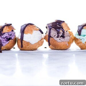 Row of four Gluten-Free Profiteroles stuffed with different colors of ice cream and drizzled with chocolate sauce on a white background