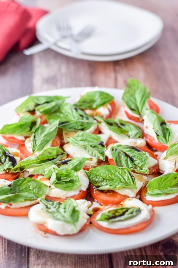 White plate with the tomato, basil and cheese salad with two other places in the background