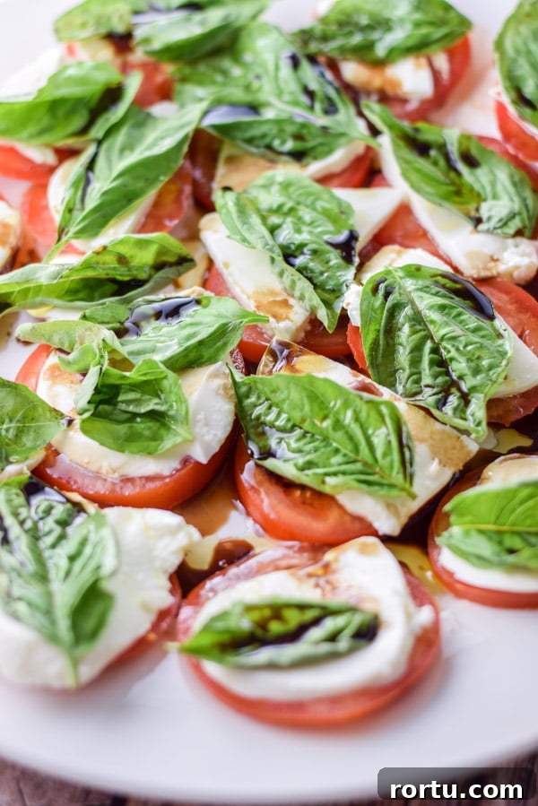 A white plate with tomatoes topped with cheese, basil and balsamic vinegar