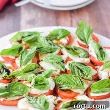 White plate with the tomato, basil and cheese salad with two other places in the background