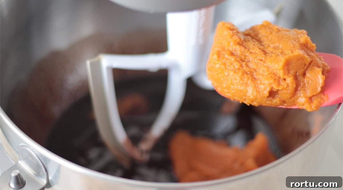 Metal mixing bowl with rubber spatula of pumpkin puree.