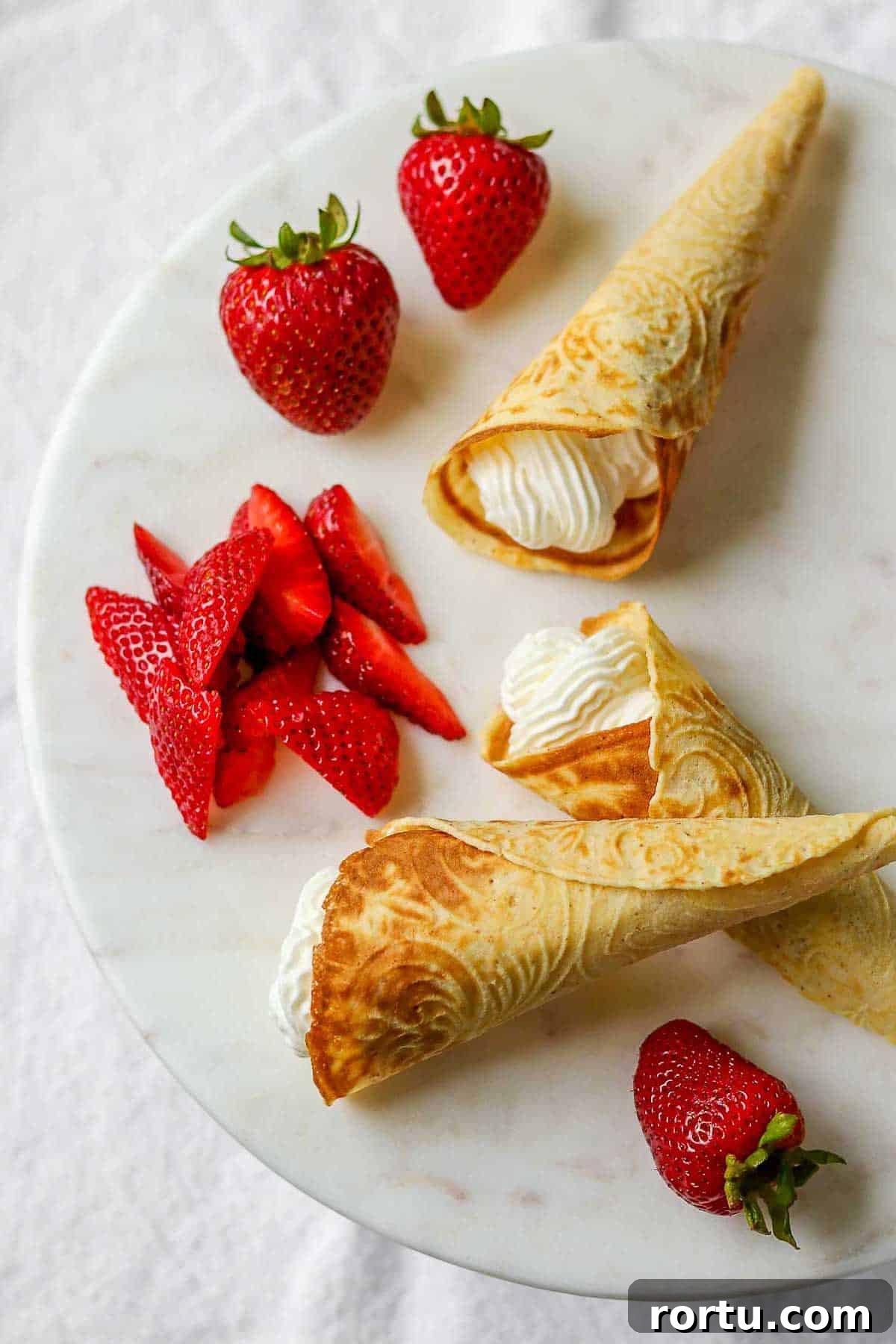 Krumkake filled with whipped cream next to fresh strawberries.