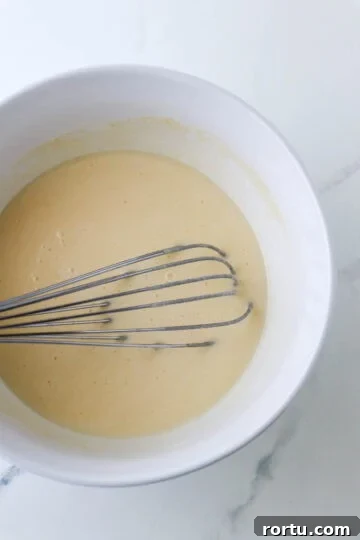 Krumkake batter in a white bowl with a whisk.