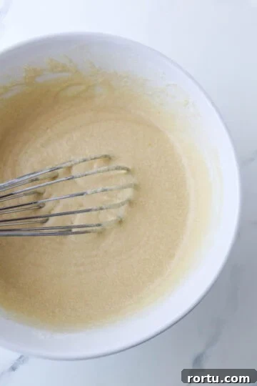 Krumkake batter in a white bowl with a whisk.