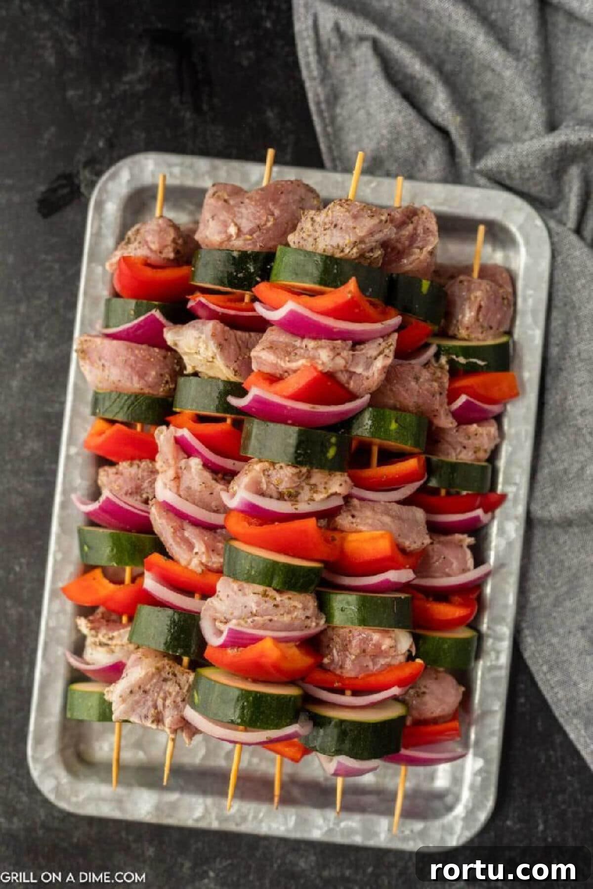 Uncooked Pork and veggie kabobs stacked on a metal platter.