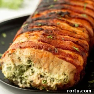 Seasoned bacon-wrapped stuffed pork loin on black plate, cooked to perfection with herbs.