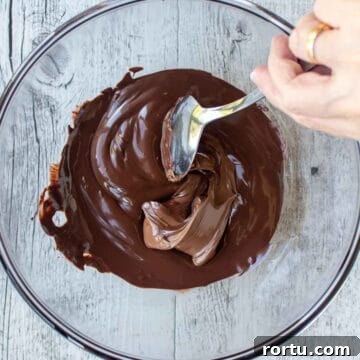 Melted chocolate and Nutella being stirred together in a glass bowl.