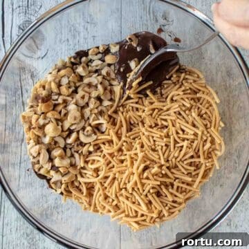 Fried noodles and chopped nuts on top of melted chocolate in a glass bowl.