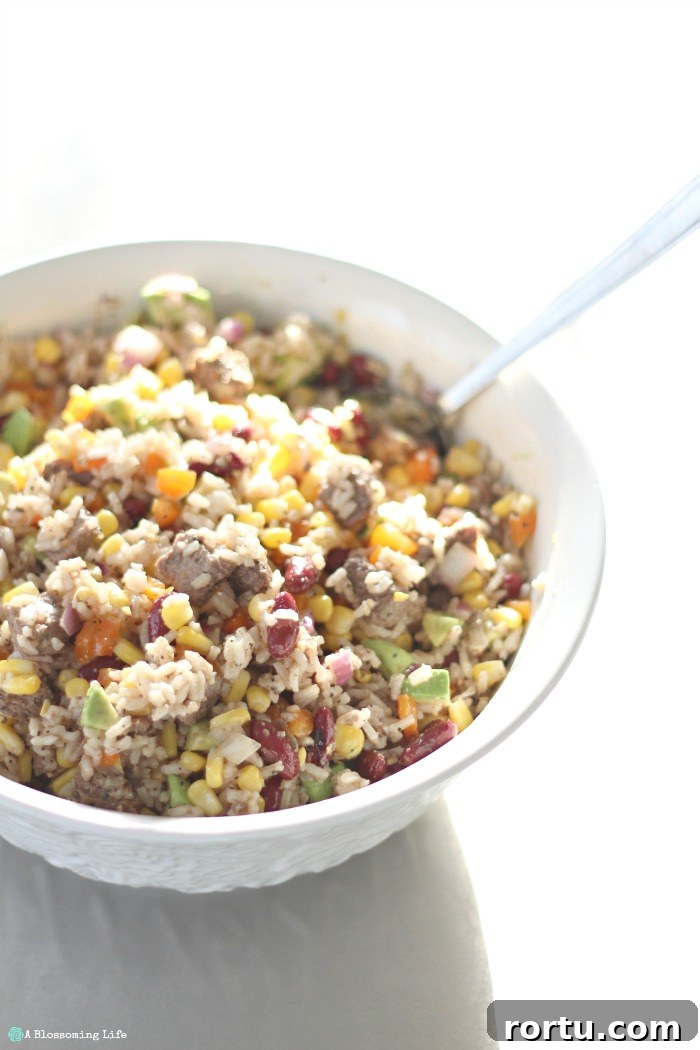 Steak and rice salad with bell pepper, corn, beans, avocado and more in a large bowl with a spoon in it