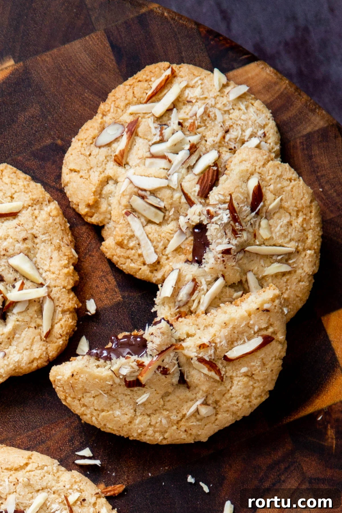 Gluten-Free Vegan Almond Joy Cookies Recipe 3 halved vegan almond joy cookies with half melted chocolate chunks peaking out on a wooden board