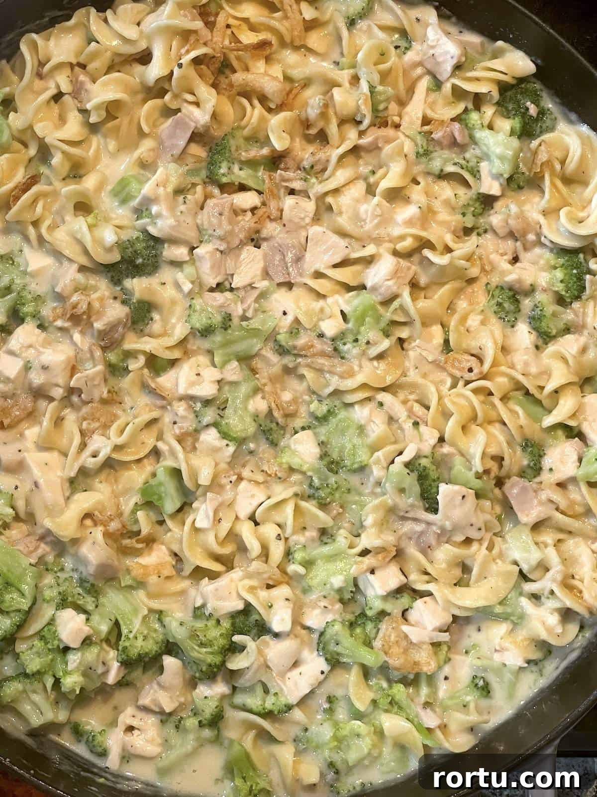 A cast iron pan with cheesy chicken casserole in it before the topping is added.