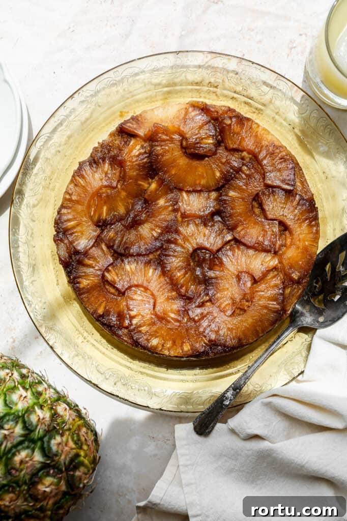 a gluten free pineapple upside down cake on a yellow glass plate next to a ripe pineapple and a glass of pineapple juice