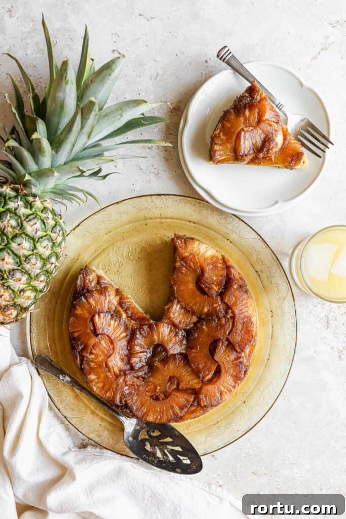 a gluten free pineapple upside down cake on a yellow glass plate next to a ripe pineapple and a glass of pineapple juice