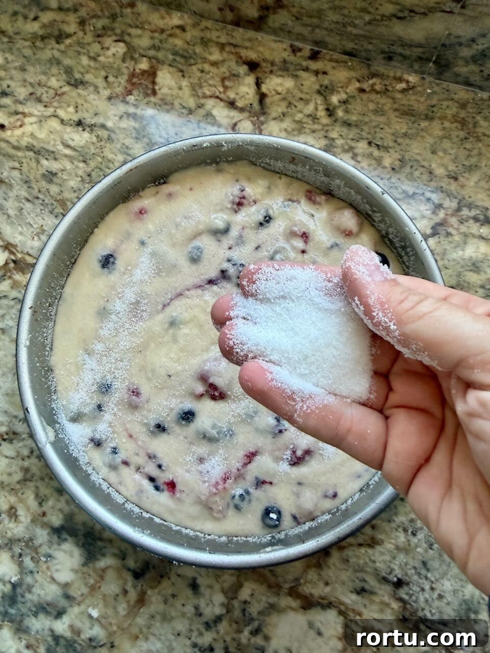 Sugar being sprinkled evenly over the surface of the cake batter.