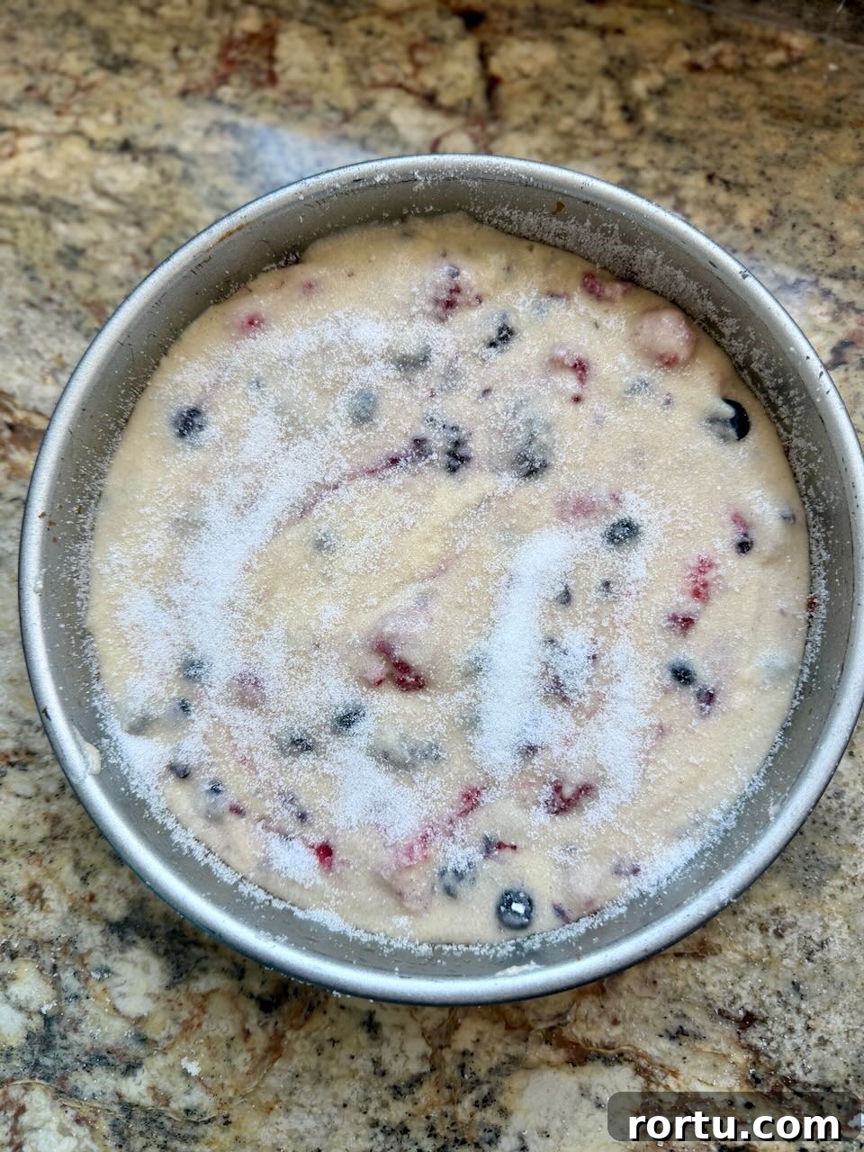 Unbaked sourdough berry cake batter in a round pan, topped with a layer of sugar.