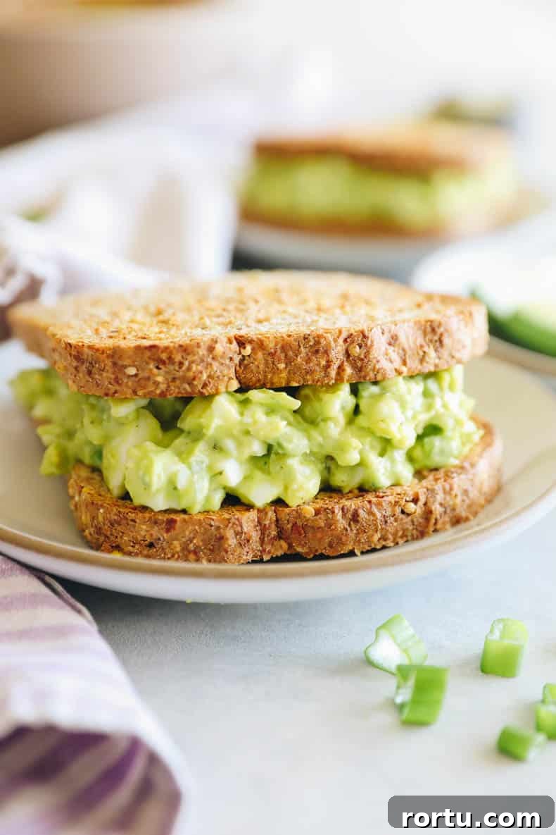 Creamy Avocado Egg Salad Recipe for Quick Lunch or Brunch 6 avocado egg salad between two slices of bread on a white plate.