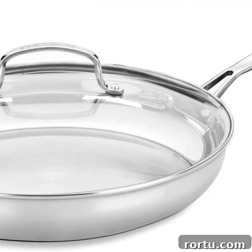 A stainless steel frying pan with a long handle and a transparent glass lid, shown on a plain white background.