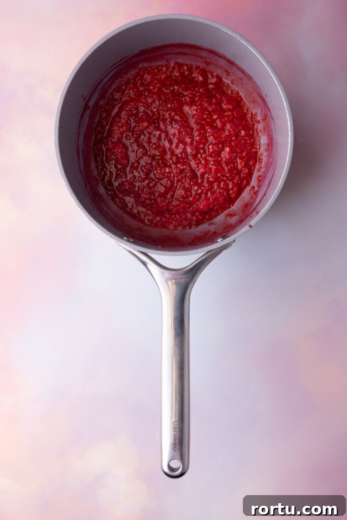 Boiled raspberries broken down into a jam in a pot.