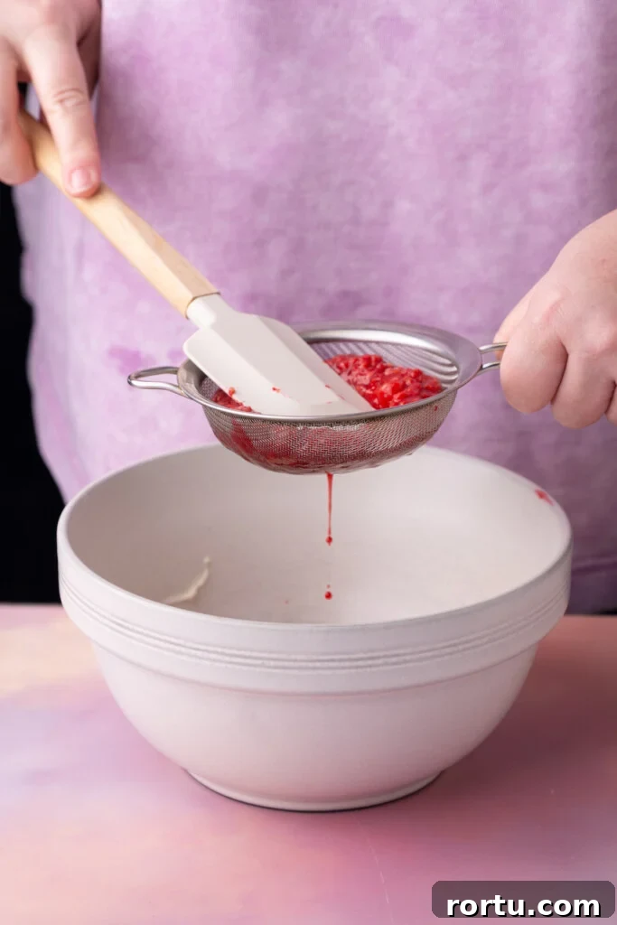 Straining boiled raspberries through a sieve to extract the juice.