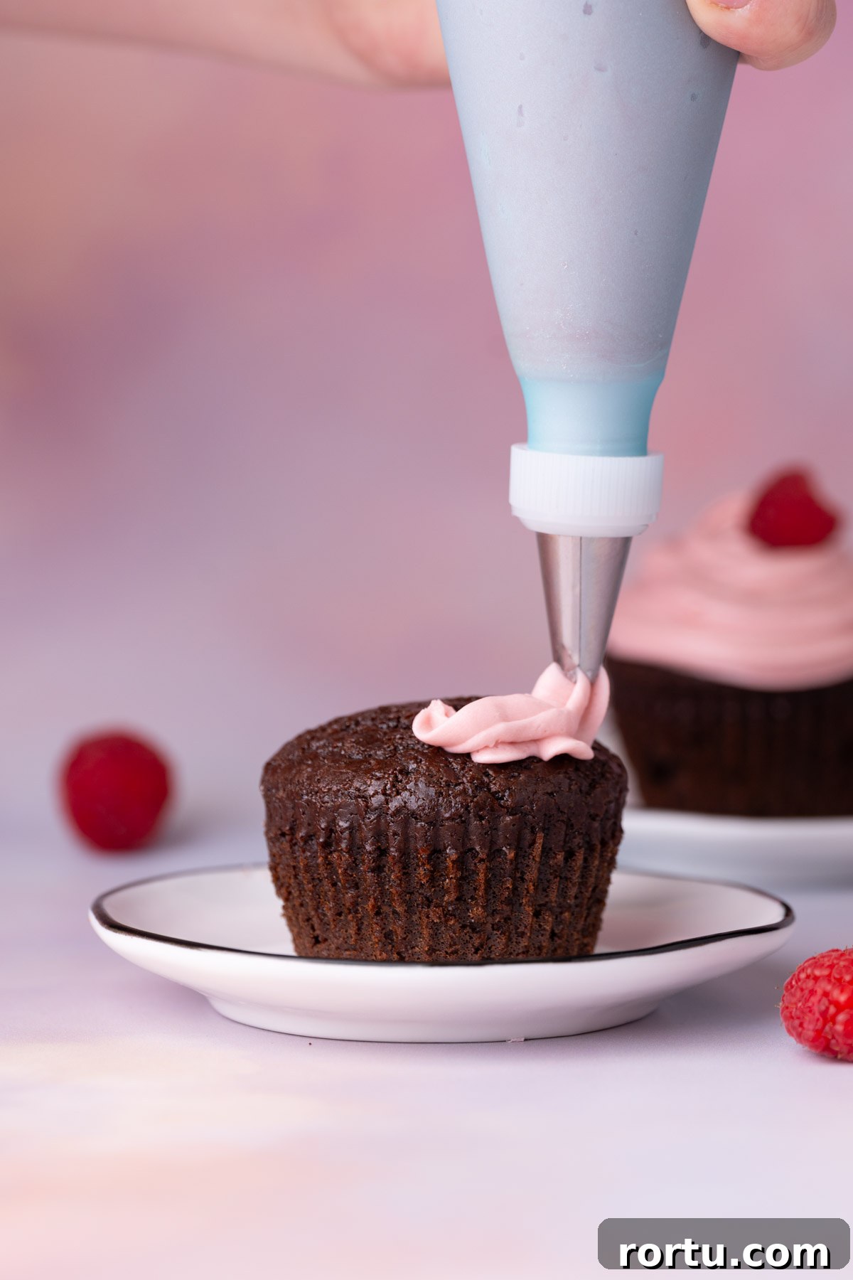 Using a piping bag to pipe raspberry frosting onto chocolate cupcakes.