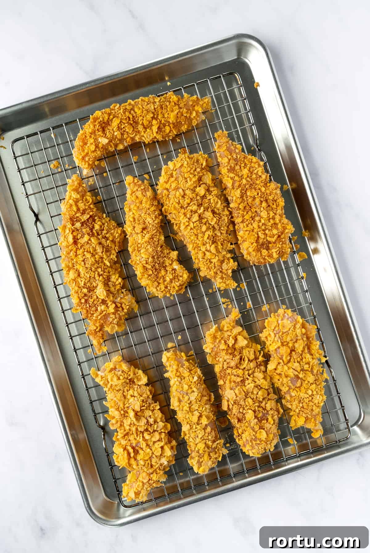 Crispy Baked Cornflake Chicken Tenders Recipe 5 Cornflake Chicken Tenders on a white rack on a baking sheet.