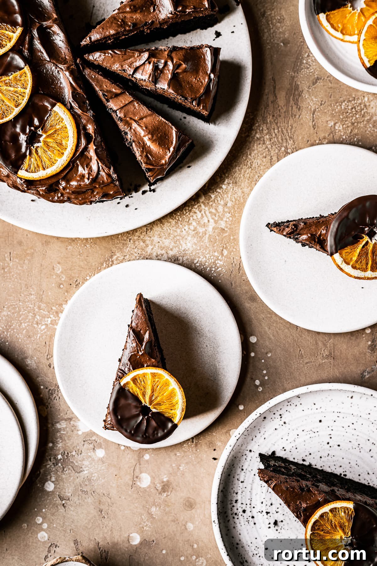Sliced chocolate orange cake on plates topped with chocolate dipped dried orange slices.