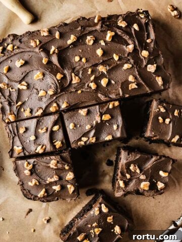 A single layer square chocolate cake on brown parchment paper with nuts sprinkled on top of whipped chocolate ganache frosting.