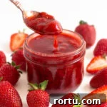 Spoonful of strawberry compote being lifted out of a glass jar surrounded by fresh strawberries.