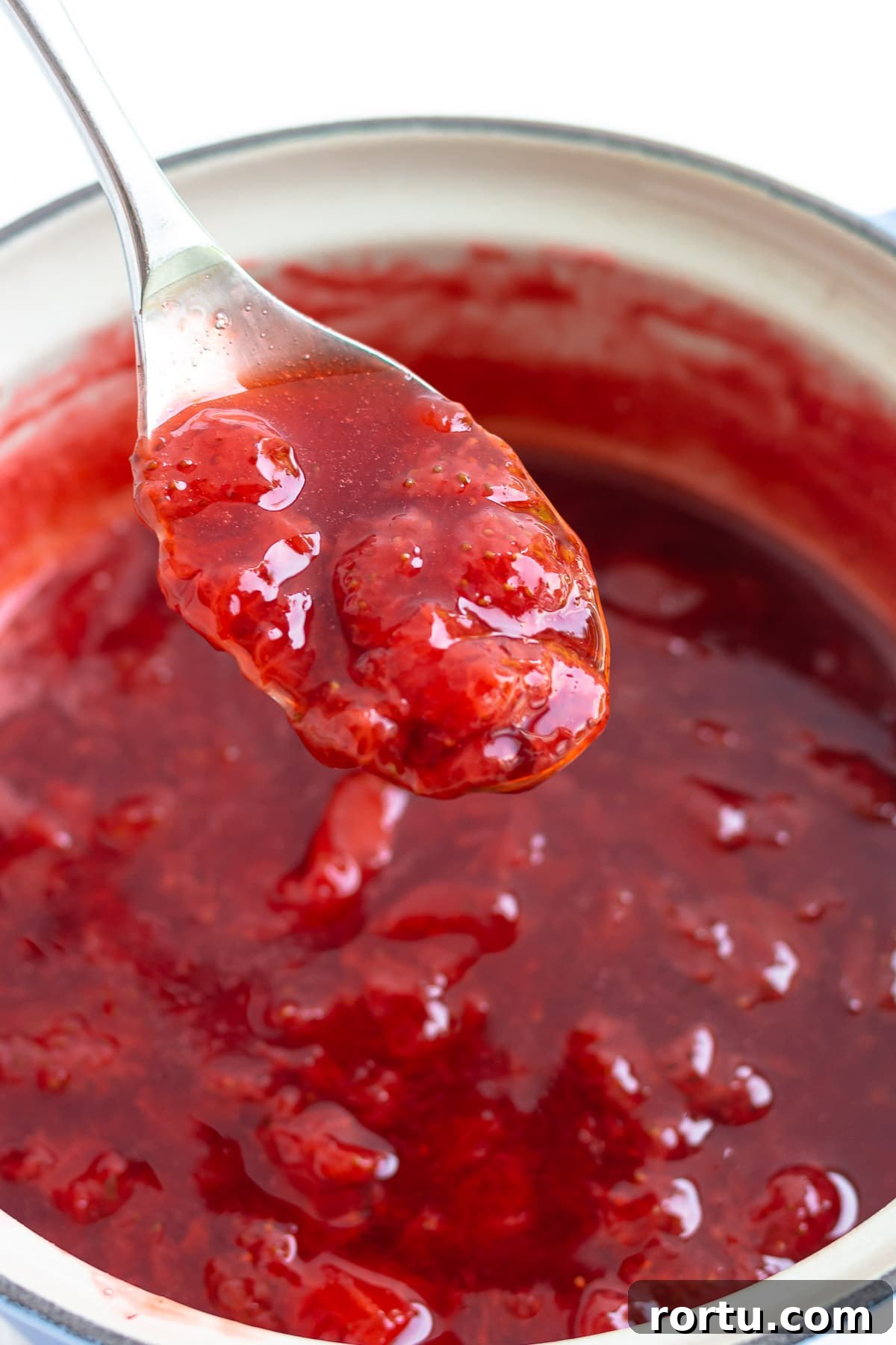 Spoon lifting homemade strawberry compote out of saucepan.