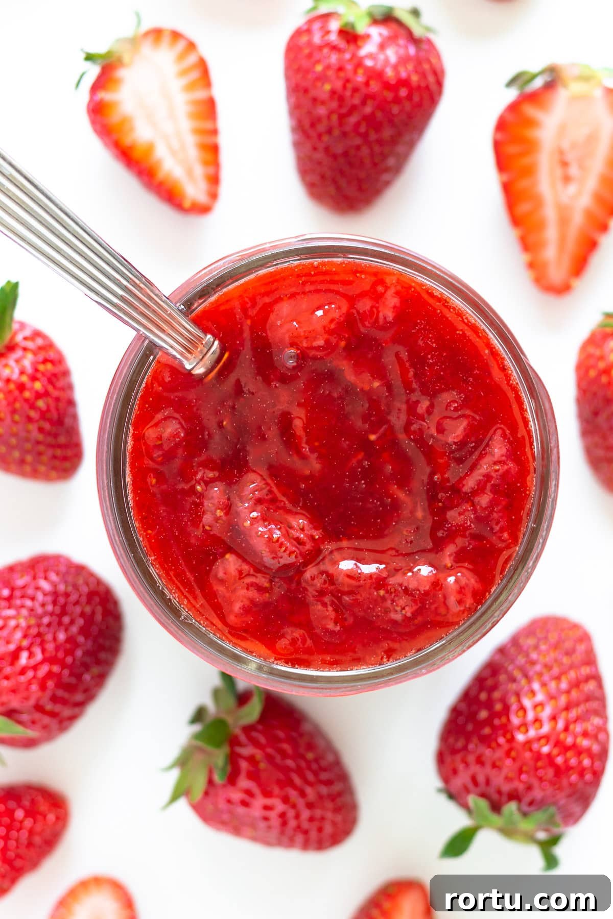 Overhead of strawberry sauce in a jar surround by fresh strawberries.