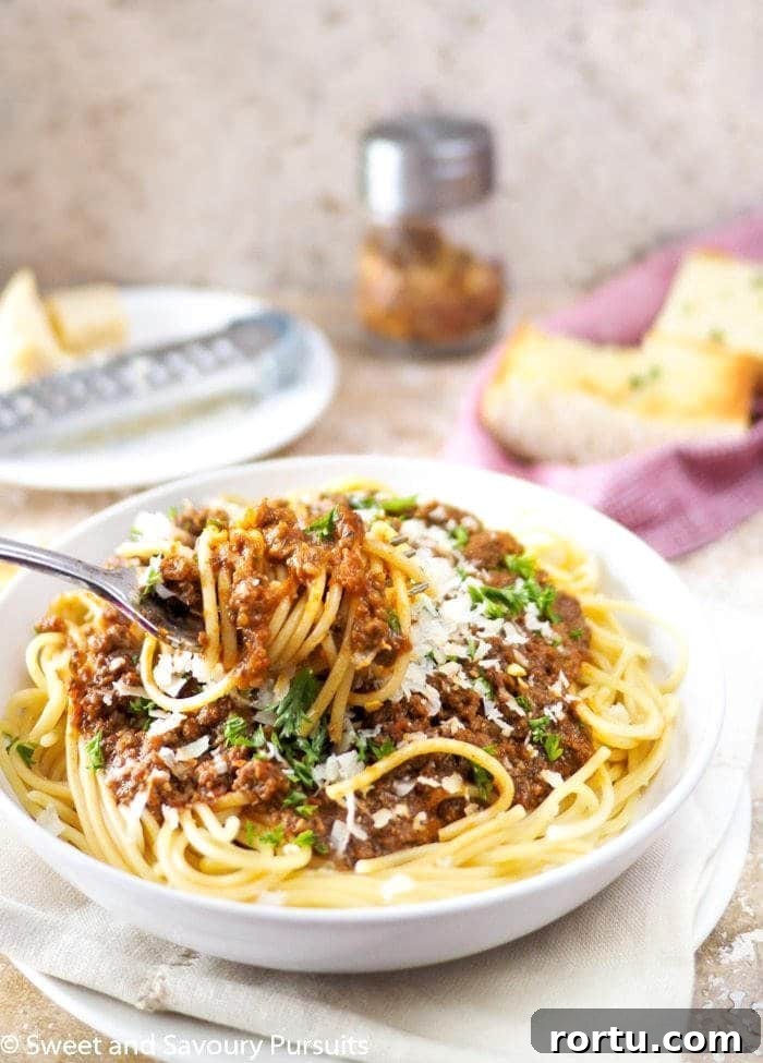 Close-up of spaghetti and meat sauce twirled around a fork. Garlic bread in background. 
