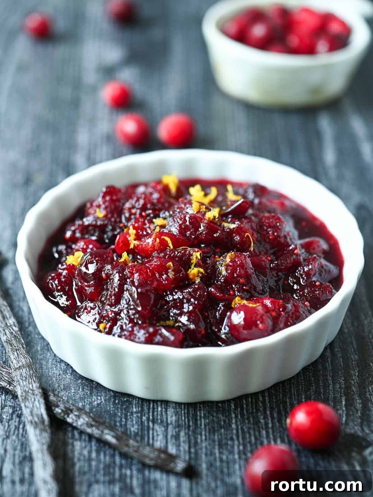 Cranberry compote in a white ramekin with cranberries and vanilla beans beside it.