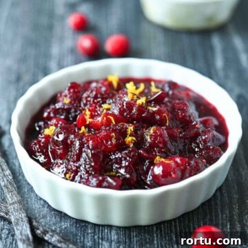 Cranberry compote in a white ramekin with cranberries and vanilla beans beside it.