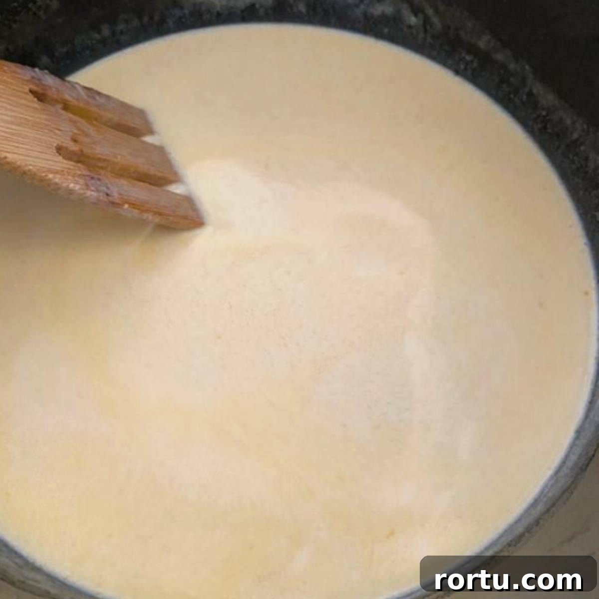 Creamy White Cheddar Macaroni and Cheese Recipe 6 Wooden spoon stirring cream in skillet.