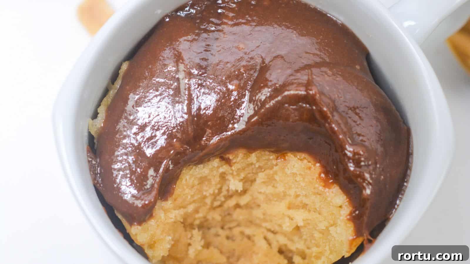 A peanut butter mug cake topped with a smooth, glossy chocolate sauce, viewed from above.