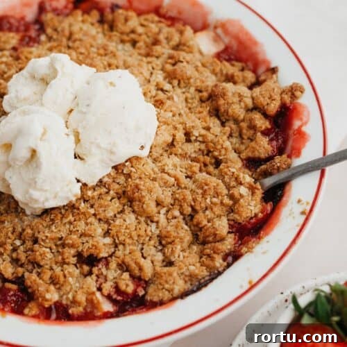 Strawberry and apple crisp in a white pie dish with several scoops of vanilla ice cream in the middle.
