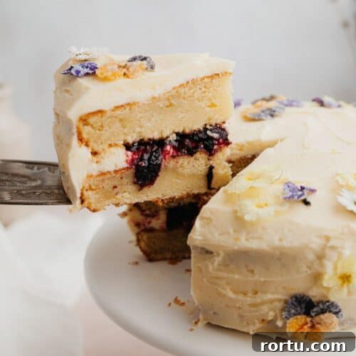 A yellow cake with a blueberry filling, a silver cake server is lifting one slice out.
