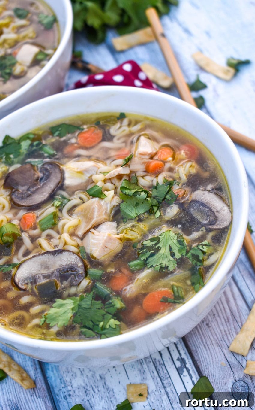 Asian chicken noodle soup in a white bowl with wooden chop sticks on the side