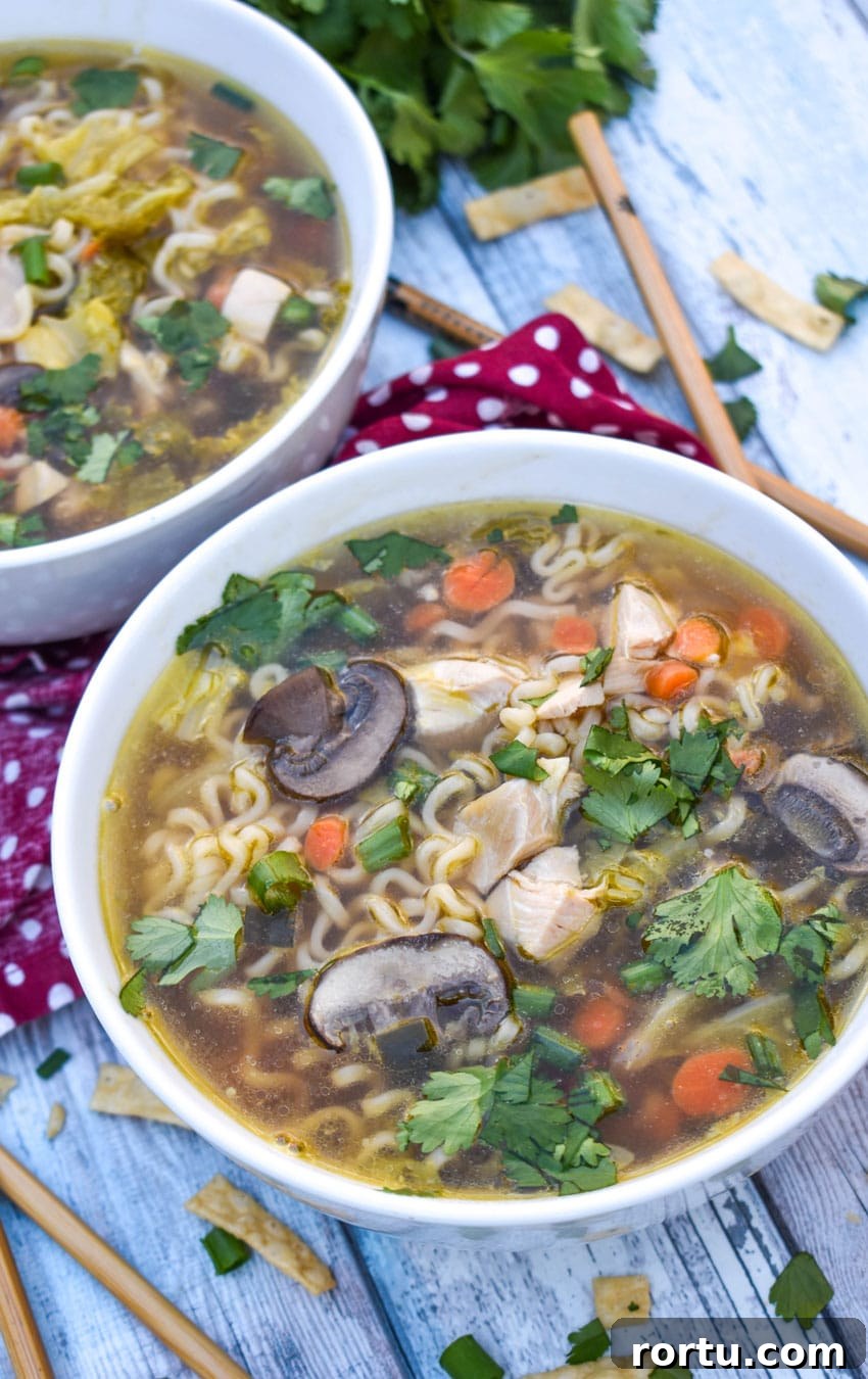 Asian chicken noodle soup in a white bowl with wooden chop sticks on the side