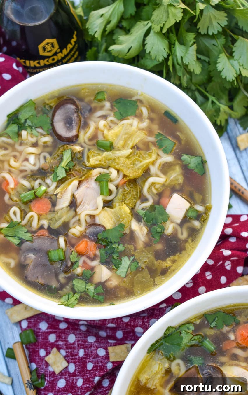 Asian chicken noodle soup in a white bowl with wooden chop sticks on the side