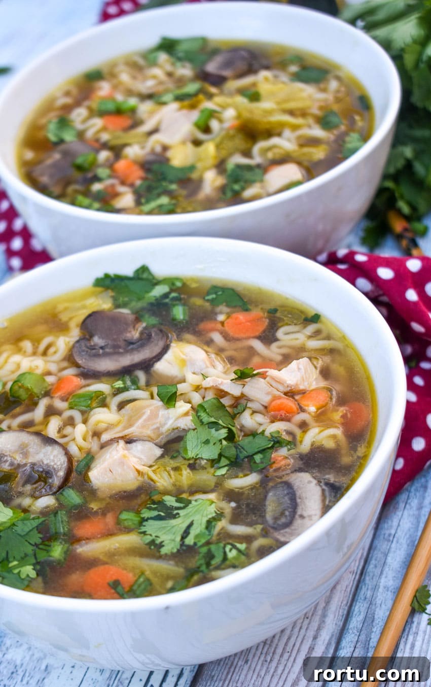 Asian chicken noodle soup in a white bowl with wooden chop sticks on the side