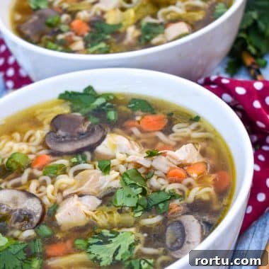 Asian chicken noodle soup in a white bowl with wooden chop sticks on the side