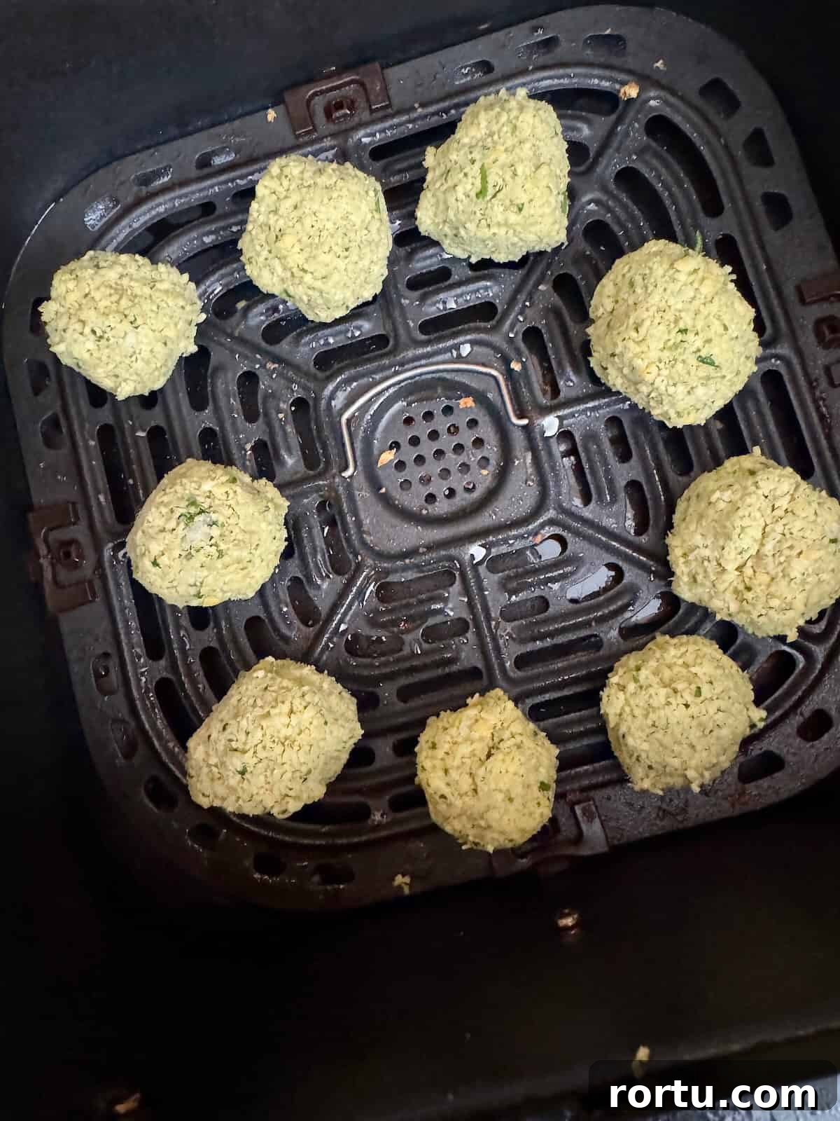 Uncooked falafel balls placed in an air fryer basket before cooking.