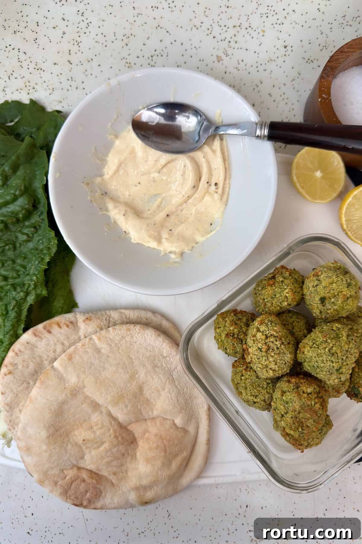 Ingredients for assembling falafel pita, including lettuce, sauce, and fresh falafel.