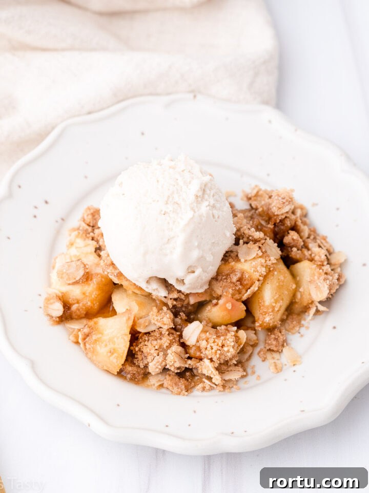 Gluten free apple crisp on a white plate topped with a scoop of vanilla ice cream.
