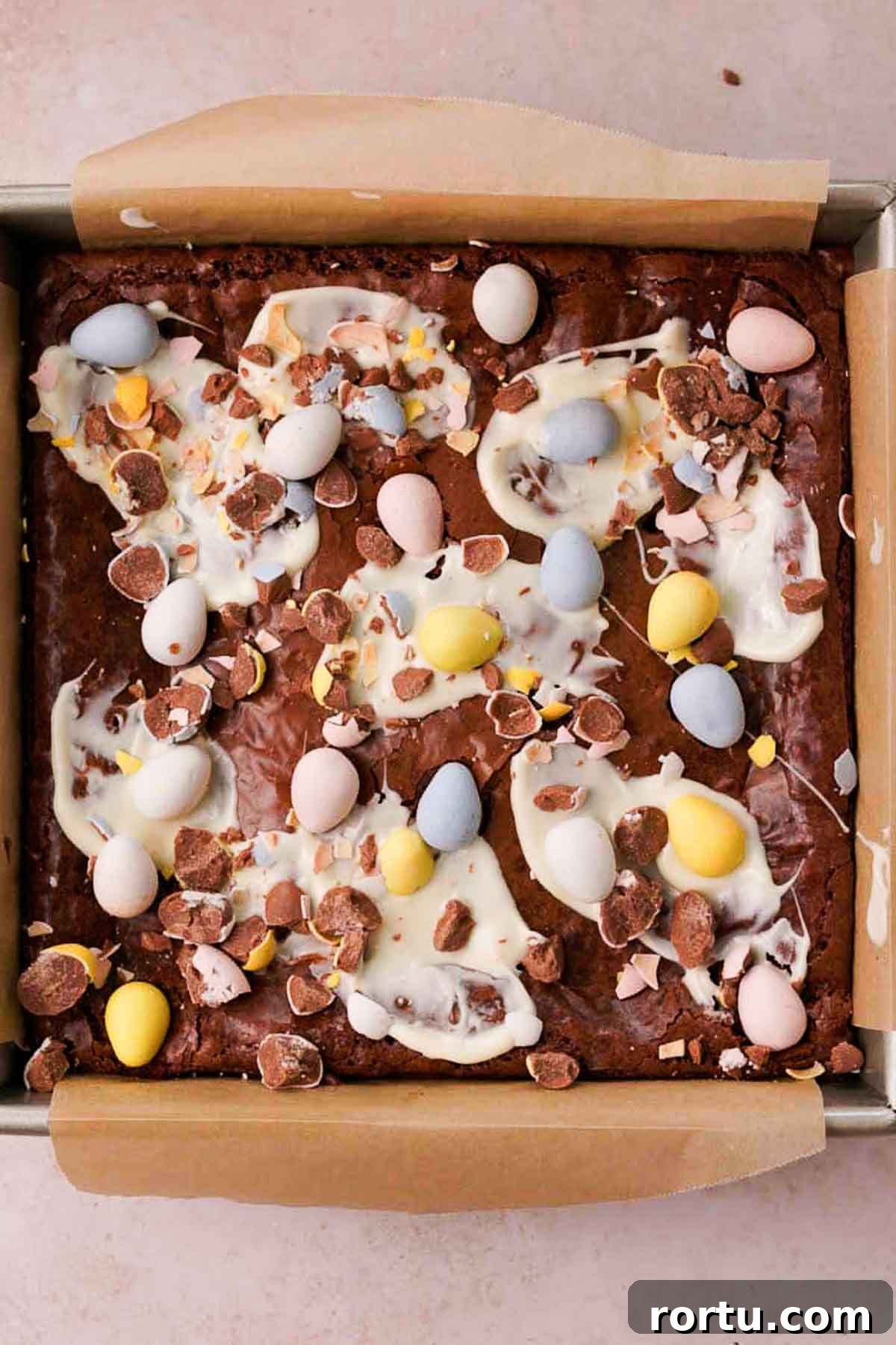Mini Egg Chocolate Brownies with Melted Candy Centers 12 mini egg brownies in square pan with smears of white chocolate and crushed mini eggs