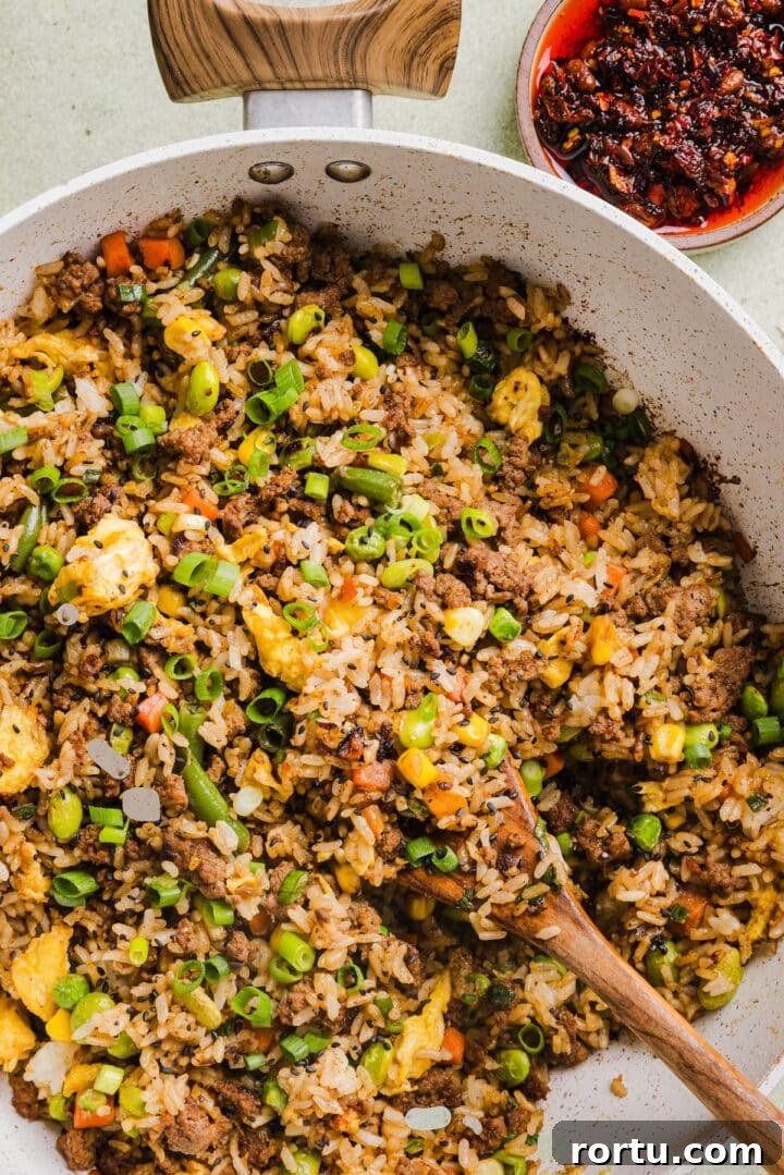 Savory Ground Beef Fried Rice Recipe for Weeknight Dinners 2 Ground beef fried rice in a large saute pan with a wooden spoon.