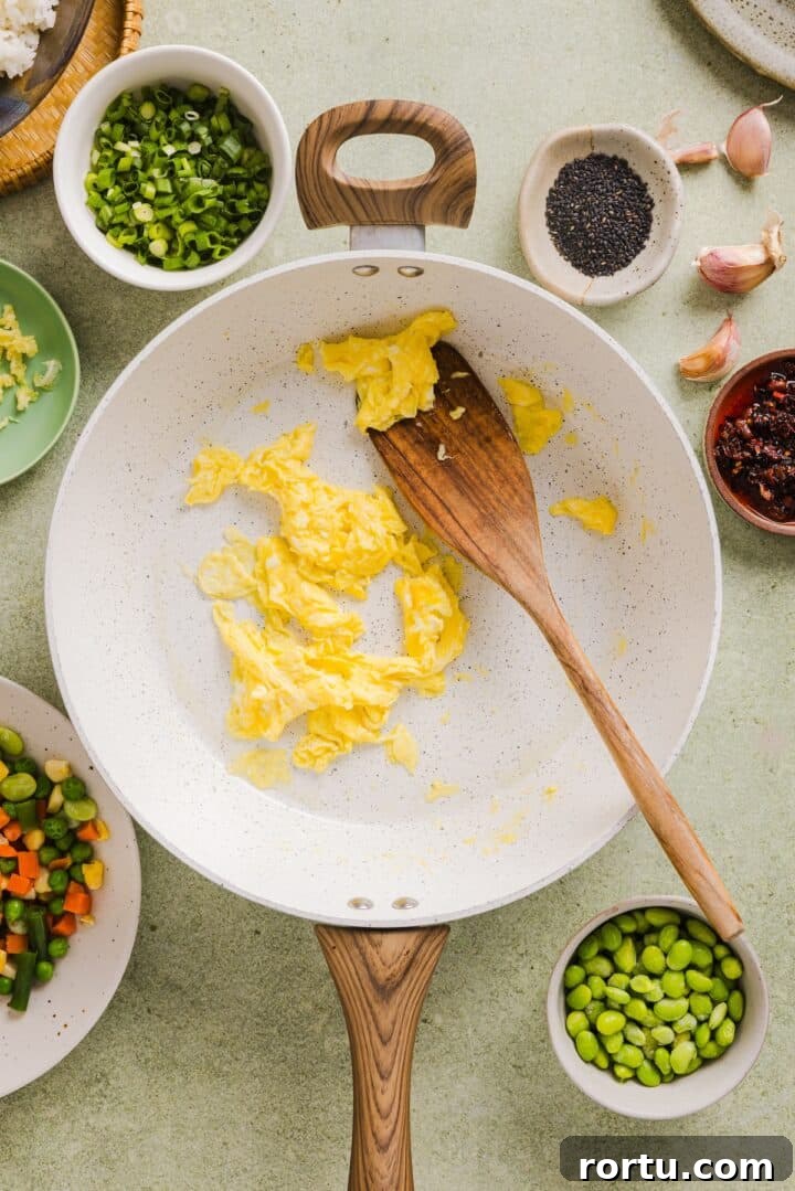 Savory Ground Beef Fried Rice Recipe for Weeknight Dinners 5 Eggs scrambled in a white pan with a wooden spoon.